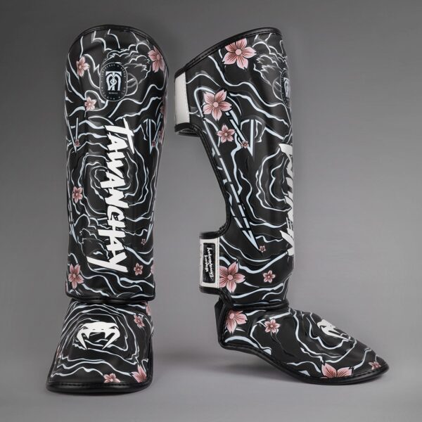 מגני רגליים מקצועיים Venum x Tawanchai בצבע שחור ולבן עם סגירת סקוץ’ מתכווננת וריפוד צפוף להגנה על השוק וכף הרגל.